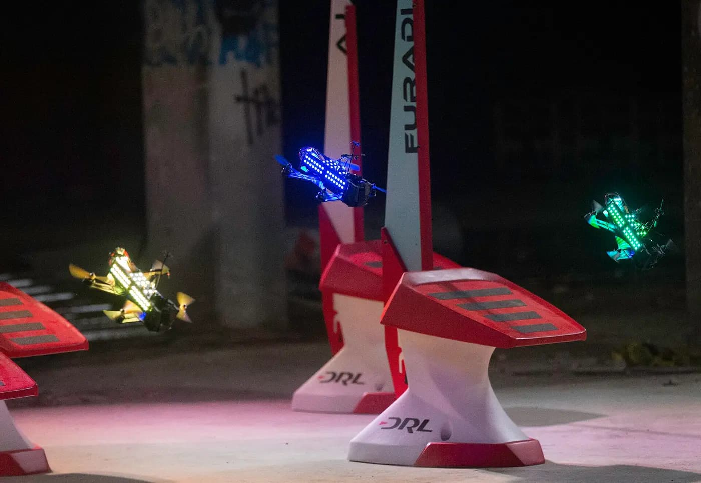 Racing drones with glowing LEDs flying between gates on a race course
