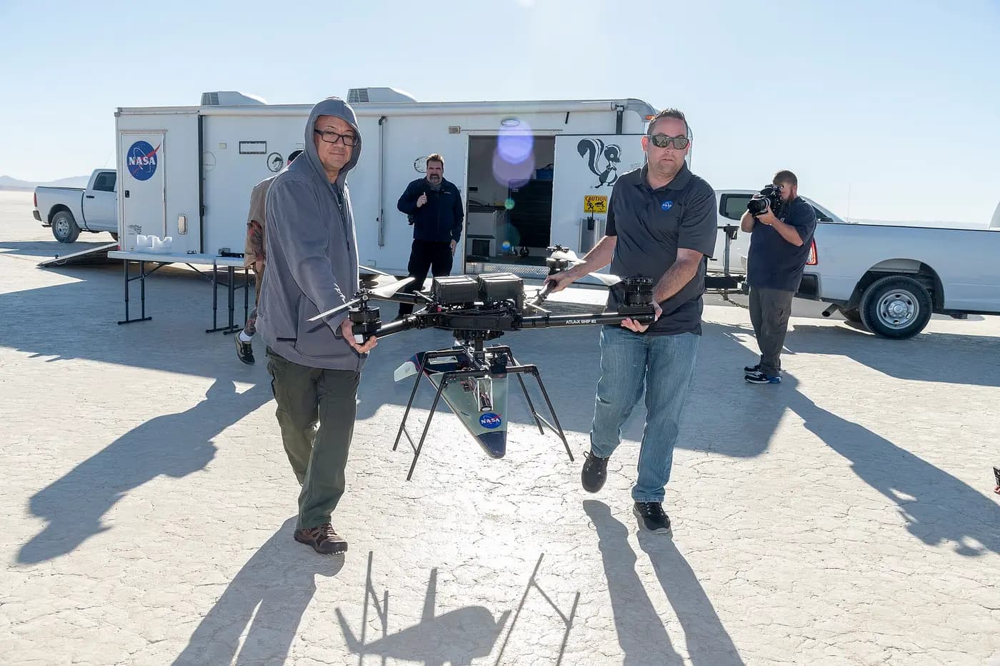 NASA researchers carrying a large research multirotor across a dry lakebed