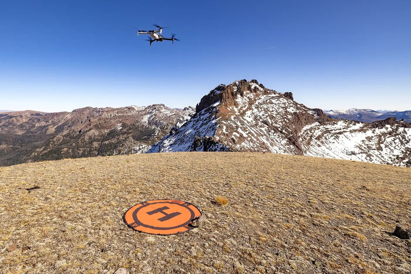 Search-and-rescue drone lifting off from a landing pad on a mountain ridge